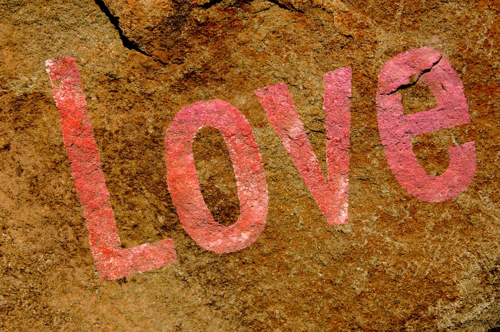 The word 'LOVE' painted in bold, pink letters on a rugged brown rock surface, showcasing a slightly weathered and enduring appearance