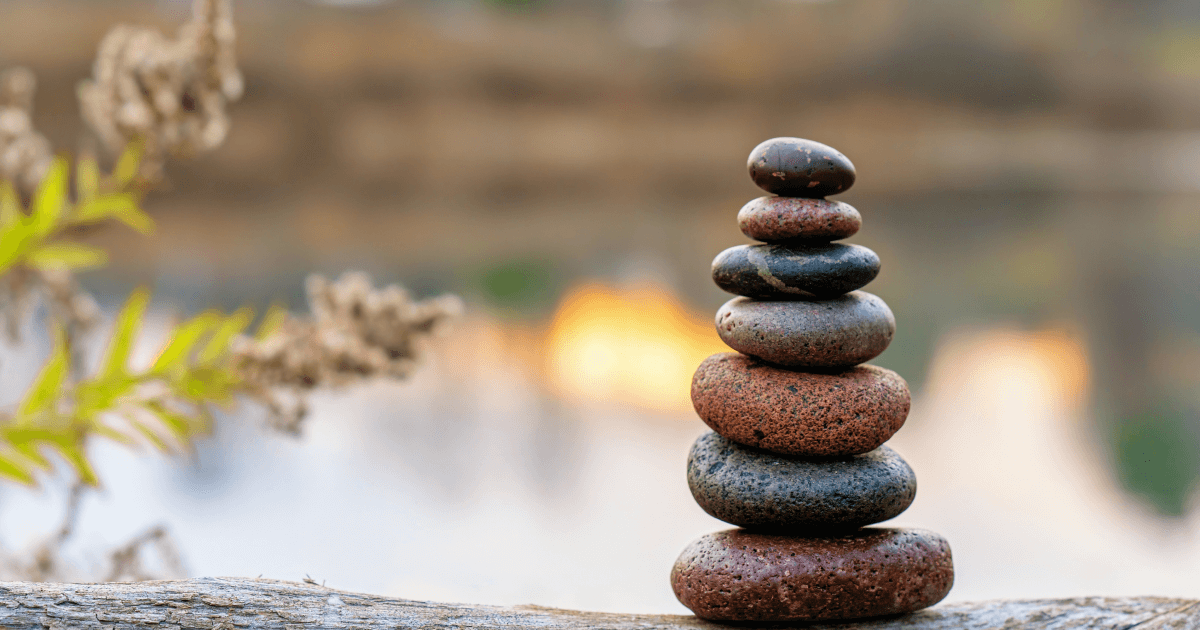 Zen-like arrangement of smooth, stacked river stones in a balanced tower, set against a soft-focus background of a blurred water scene, symbolizing the principles of Hun Yuan Chi. The harmony and stability of the stones reflect the essence of Wisdom Healing Qigong and sound healing, embodying the flow of source energy in nature.