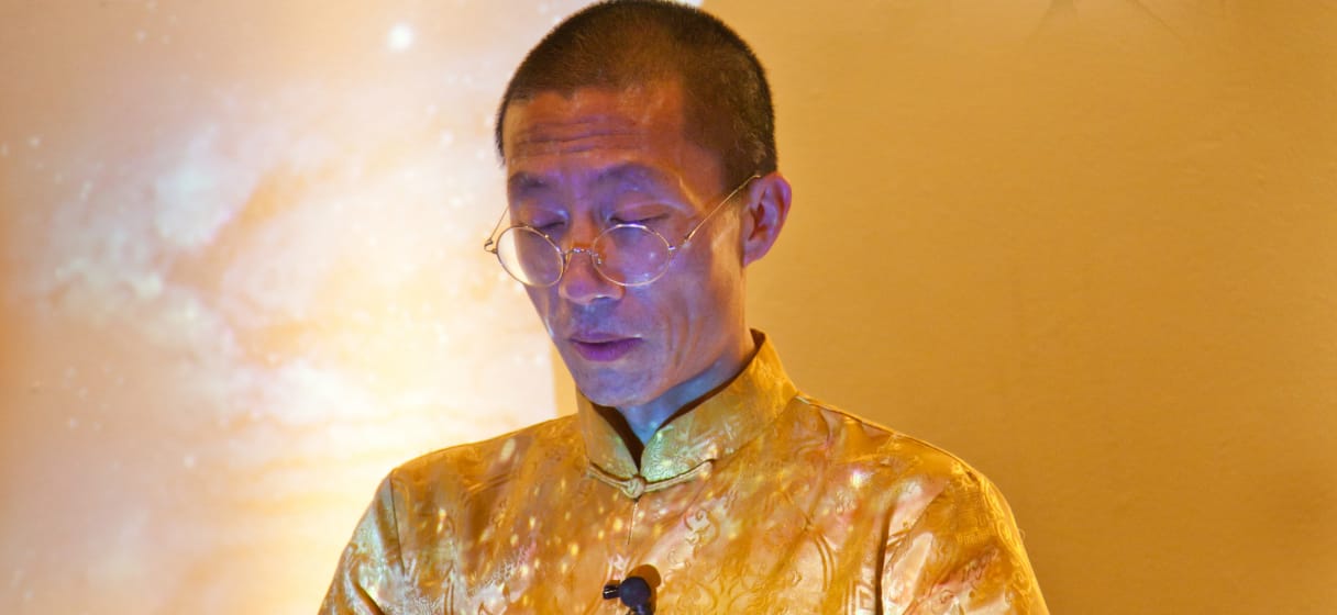 Master Mingtong Gu in a golden traditional outfit, deeply focused with a serene cosmic energy backdrop, symbolizing wisdom and introspection in healing practices.