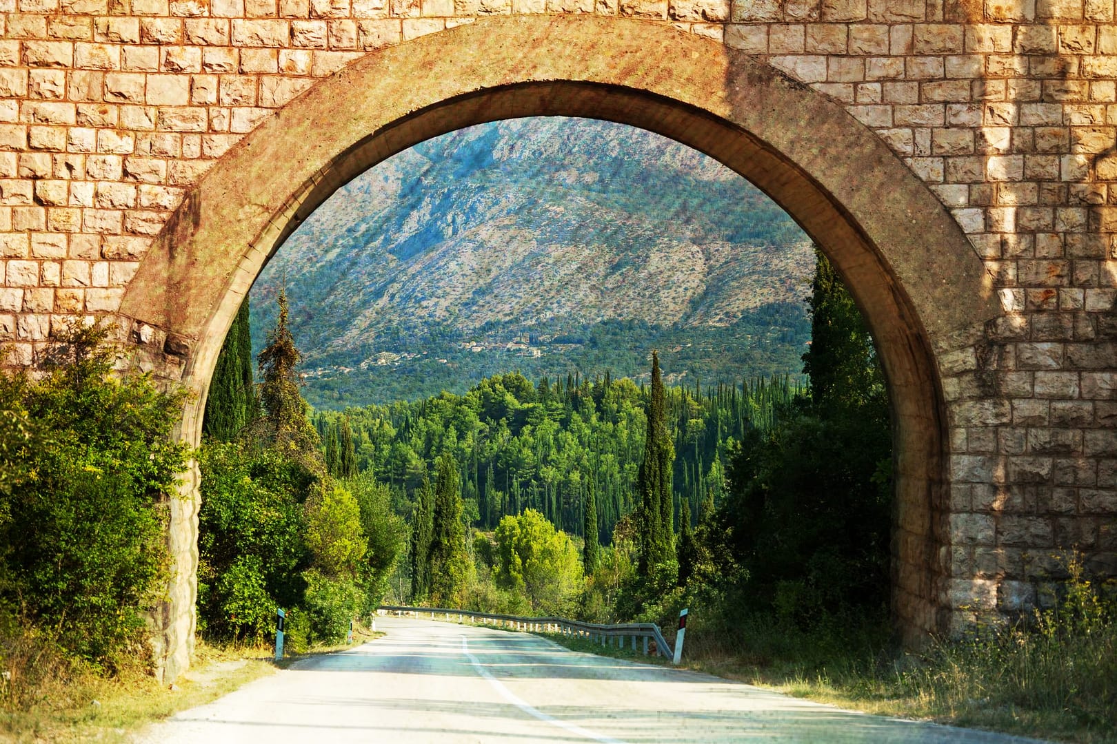 A stone arch over a road leading to a mountain.