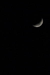 A crescent moon glowing softly against a dark, starless night sky, showcasing its craters and surface details in a serene celestial view.