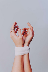 Two hands intertwined, adorned with delicate rings, wrapped at the wrists with white cloth, symbolizing the overcoming of trauma through life mastery and the energy balance of Qigong, set against a soft pastel background.