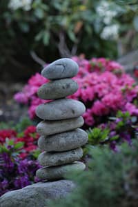 A balanced stack of smooth stones set against a vibrant background of blooming pink flowers, symbolizing harmony, grounding, and tranquility, ideal for the Spring 2024 Mini-Retreat Series.