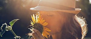 A woman in a hat smelling a sunflower.