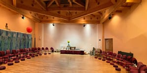 Interior of the Kiva, a spacious circular meeting room with wooden beams, arranged chairs, meditation cushions, and a serene altar, creating a peaceful and welcoming space for gatherings and practices.