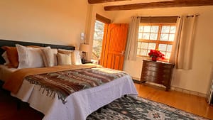 Cozy and sunlit bedroom in Pueblo House #1 - APACHE, featuring Southwestern-style decor, wooden beams, a comfortable bed with patterned blankets, and a warm, rustic ambiance.