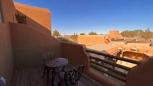 Private rooftop balcony with wrought iron table and chairs overlooking traditional adobe architecture and scenic desert landscape at The Zia Apartment.