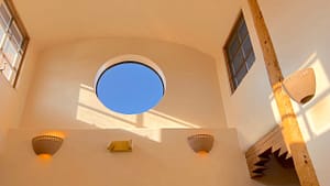 Serene architectural design at the Serenity Center featuring a circular skylight framing the blue sky, surrounded by warm, earthy tones and natural wood accents illuminated by soft wall lighting.