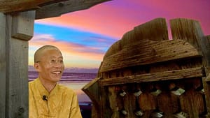 Master Mingtong Gu smiling warmly, framed by a rustic wooden gate, with a vibrant sunset over the ocean in the background, symbolizing serenity and inspiration.