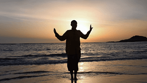 Silhouette of Master Mingtong Gu practicing Wisdom Healing Qigong at sunset on a beach, with arms raised in a meditative pose against a backdrop of a golden sky and the tranquil sea. The serene setting enhances the spiritual connection and calming energy of the Wisdom Healing Qigong practice.