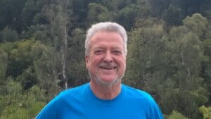 Portrait of Otis smiling warmly in a vibrant blue shirt.