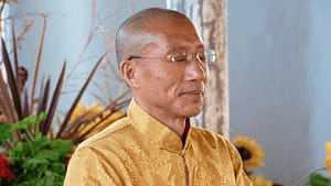 Master Mingtong Gu in a serene meditative pose, wearing a golden traditional outfit, surrounded by vibrant plants and sunflowers, symbolizing harmony, mindfulness, and a deep connection to nature.