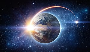 A view of Earth from space illuminated by the sun's rays, with a glowing red trail of a spacecraft orbiting the planet, surrounded by a vast star-filled galaxy.