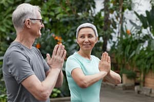 Senior man and woman practicing mindfulness and yoga together outdoors in a lush green garden, symbolizing health, connection, and wellness.