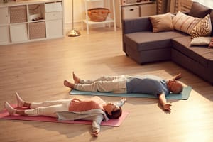 Senior couple lying in Savasana pose on yoga mats in a cozy living room, practicing relaxation and mindfulness in a warm and serene home setting.