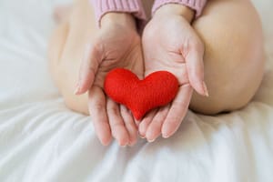 Hands gently cradling a red heart, symbolizing life mastery, healing energy, and the principles of Qigong.
