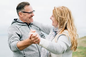 Happy middle-aged couple dancing outdoors on a breezy day, sharing a joyful moment of connection and love, with a scenic natural background.