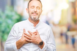 Serene man with eyes closed, placing both hands on his chest, expressing gratitude or mindfulness.
