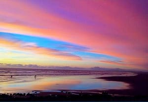 Vivid sunset over a serene beach with colorful pink, orange, and blue hues reflecting on the calm ocean water, creating a peaceful and inspiring scene.