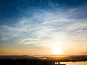Serene sunrise over a river landscape with golden light reflecting on water and expansive blue sky, capturing the peaceful energy of early morning.