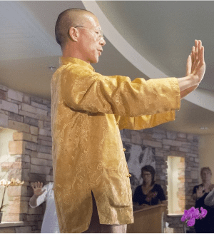 Master Mingtong Gu sitting in meditation, hands over his heart, radiating peace and energy during a Wisdom Healing Qigong session.