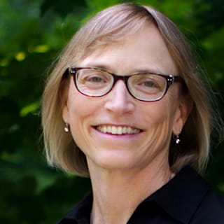 A portrait of Susan, featuring a warm smile and glasses, set against a backdrop of lush greenery.