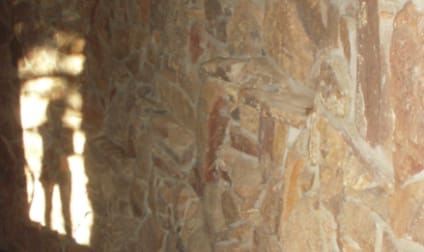 A textured stone wall illuminated by sunlight, with the soft shadow of a figure cast onto the surface. The interplay of light and shadow creates a contemplative and mysterious atmosphere.