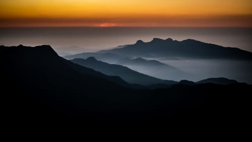 Majestic mountain silhouettes layered in the soft glow of sunrise, capturing the tranquility of nature and the beauty of dawn